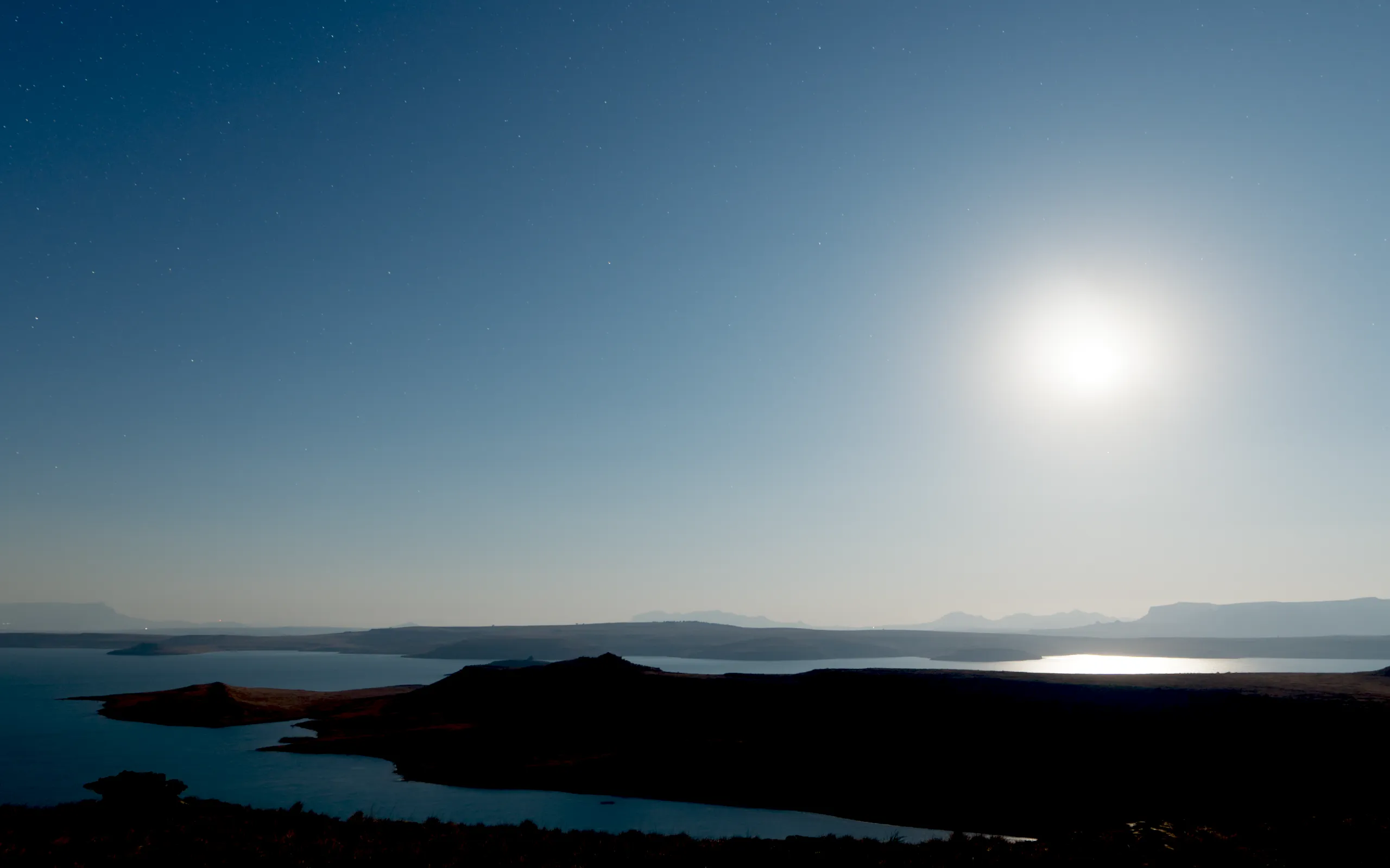 Night. The moon up over the dam and its reflection on the water, stars above, the hill black.
