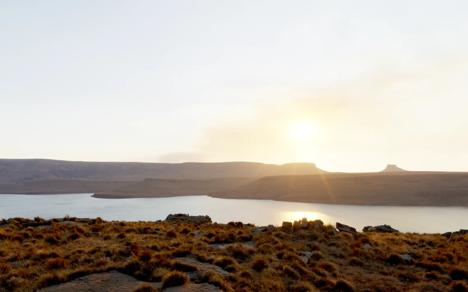 Lookout, the sun setting over a dam seen from a grass hilltop